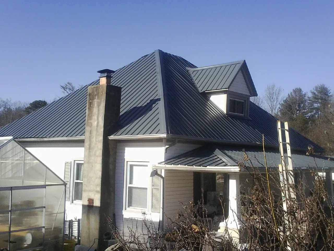 Dark blue standing seam metal roof on a white farmhouse with dormer — Slate & Tile Roof Repair by Roofing Brothers in Green Ridge