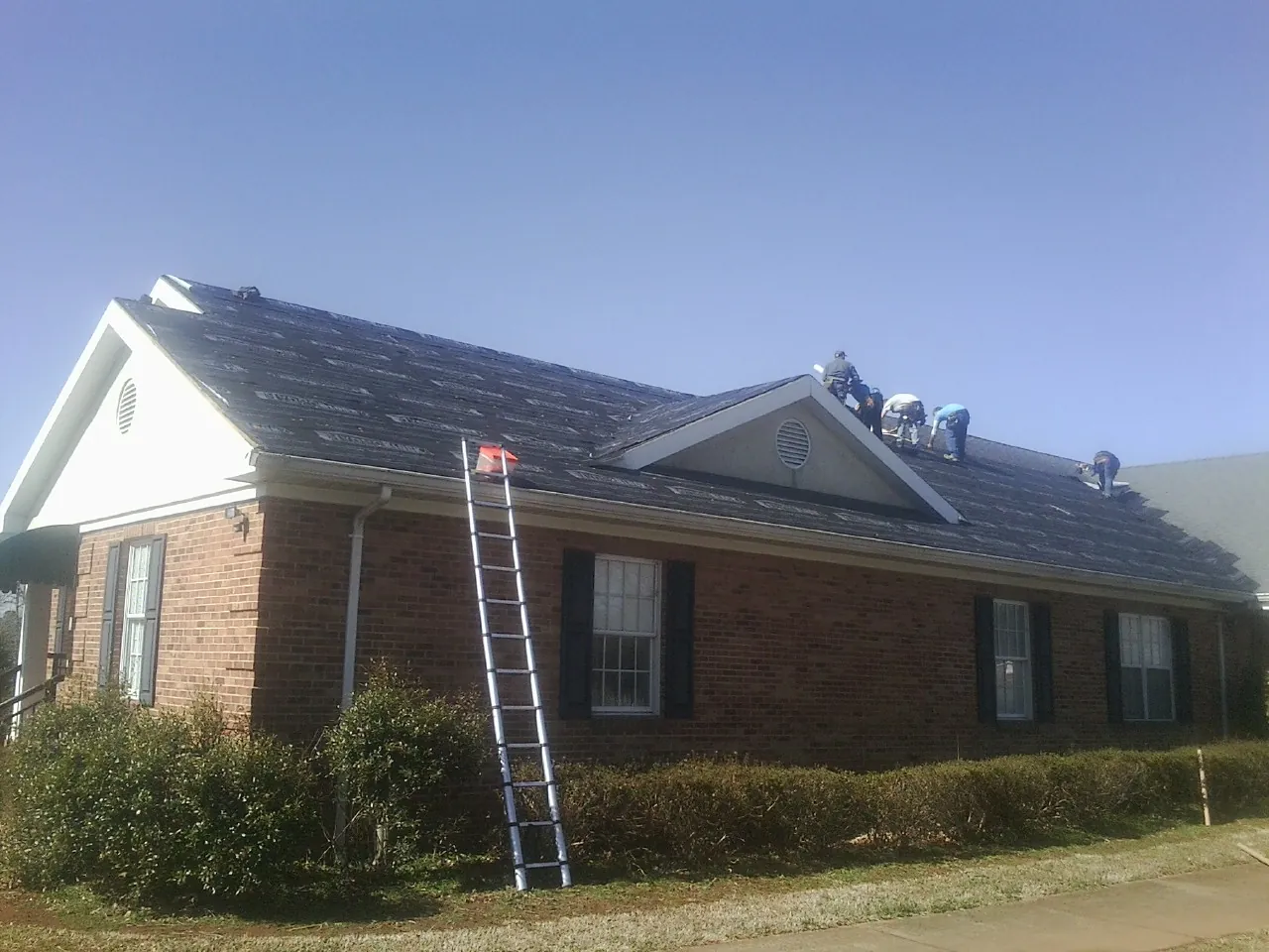 Crew tearing shingles off a brick ranch roof with a ladder set — Metal Roof Repair work by our crew in Green Ridge