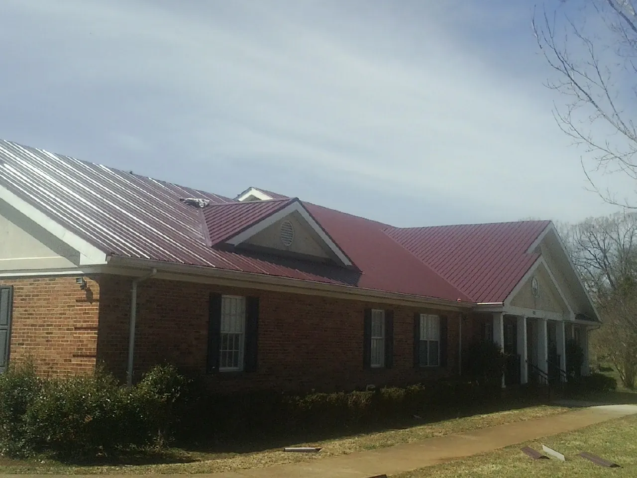 Red metal roof with gabled entries on a long brick building, from a Hail Damage Roof Repair job in Green Ridge