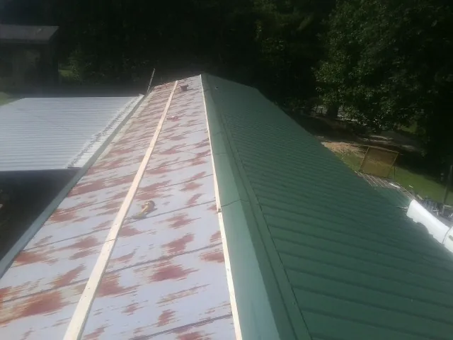 Old rusted panels beside newly installed green metal roofing — Wind Damage Roof Repair by Roofing Brothers in Green Ridge