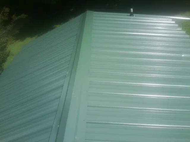 New green metal panels meeting at the ridge of a roof — Flat Roof Repair work by our crew in Green Ridge