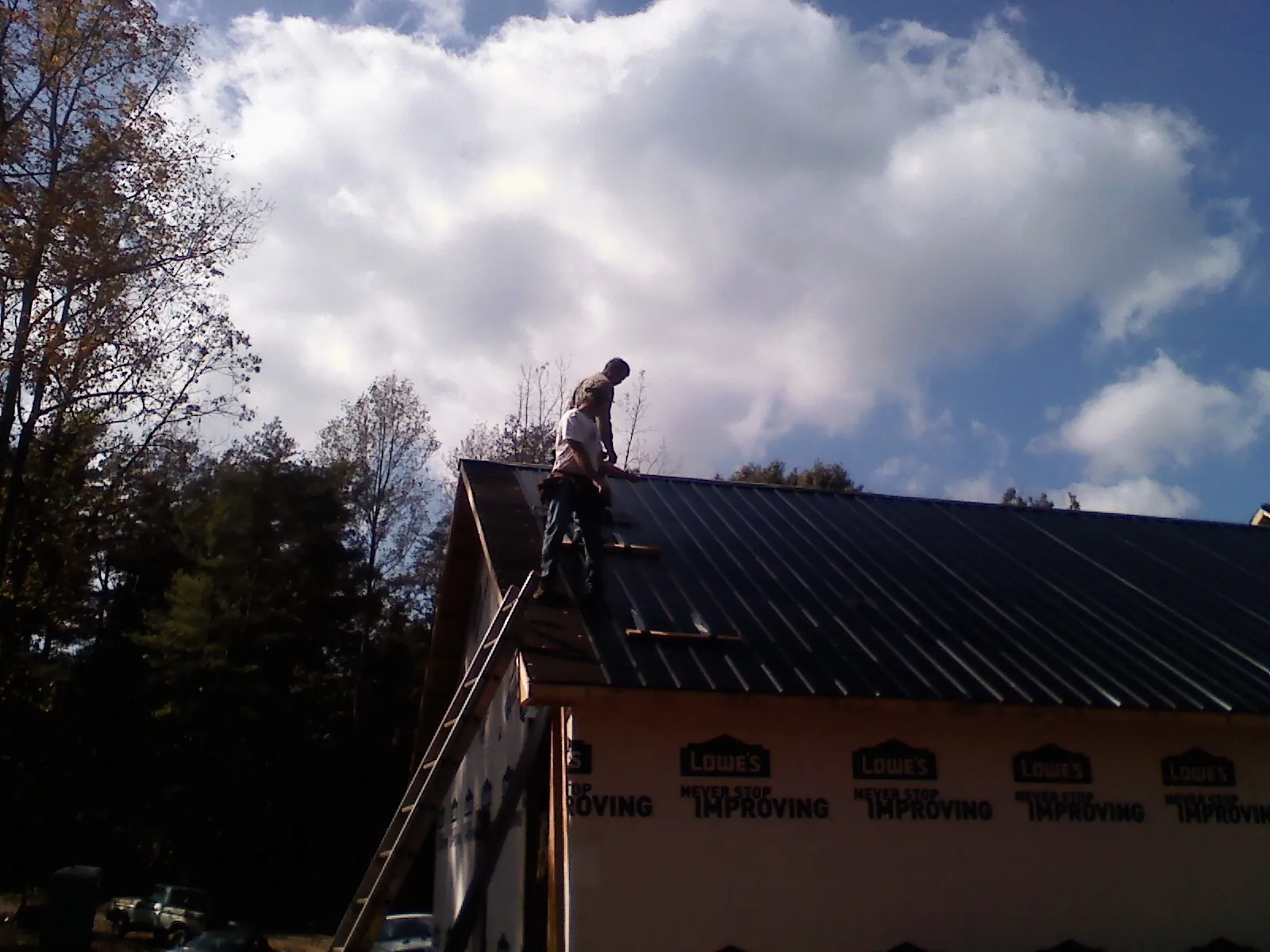 Roofer fastening dark metal panels high against a cloudy sky, from a Roof Inspection job in Green Ridge