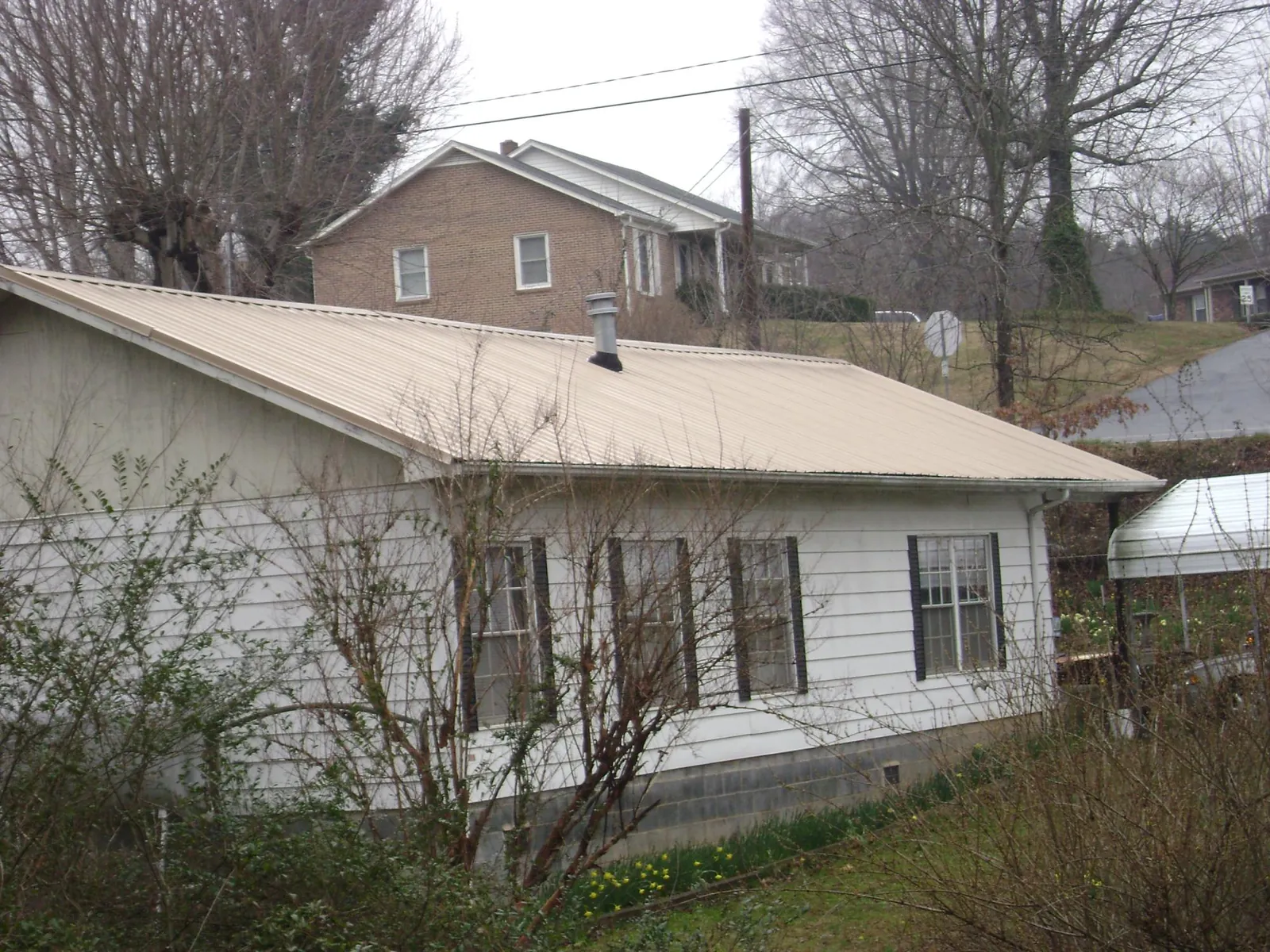 Tan metal roof on a white sided house set into a hillside — Commercial Roofing by Roofing Brothers in Green Ridge