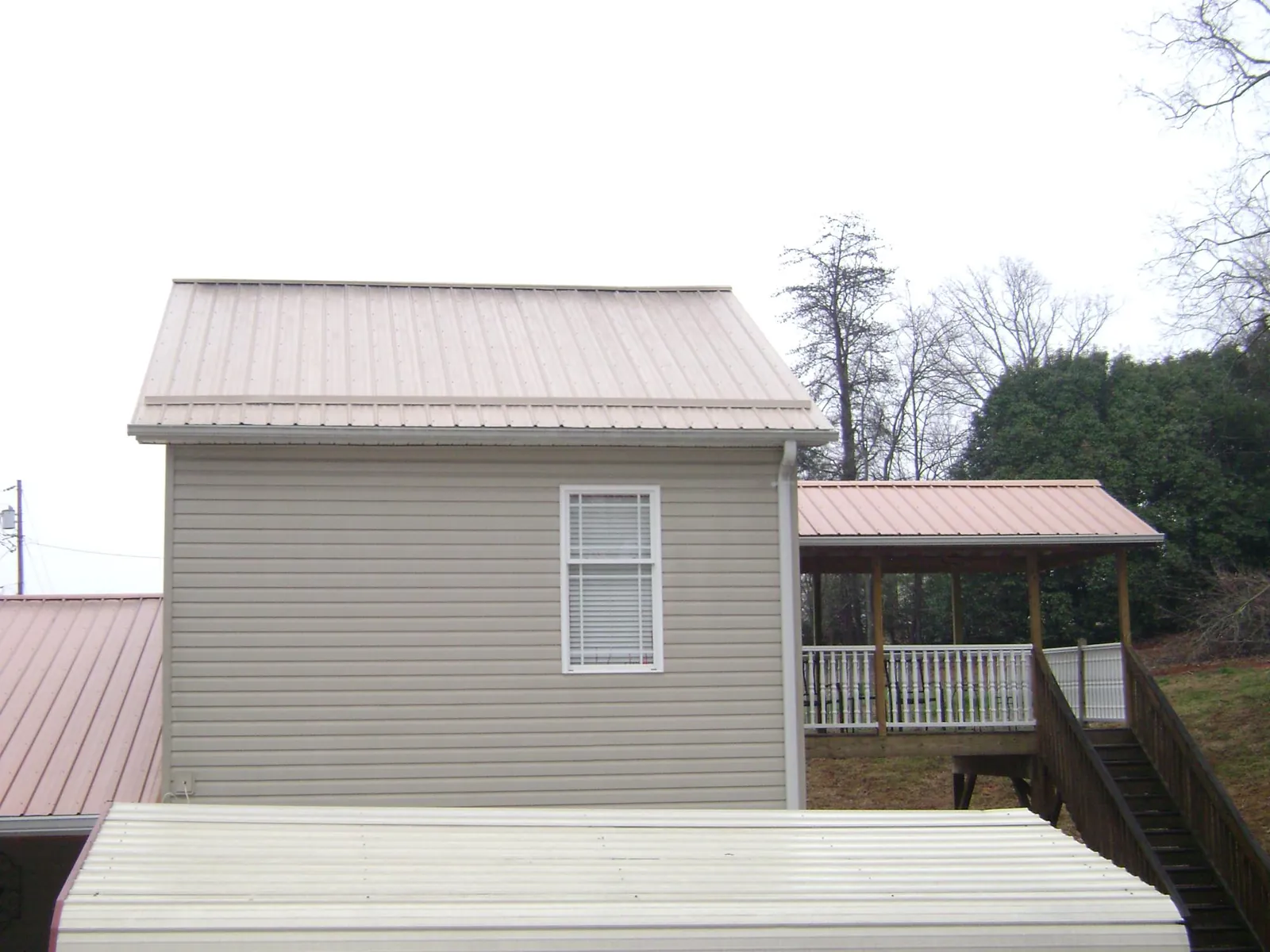 Tan metal roofs on a two story addition and attached porch, from a Roof Replacement job in Green Ridge